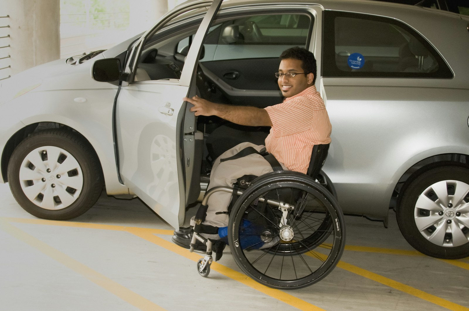 Pessoa em cadeira de rodas ao lado de um automóvel adaptado.